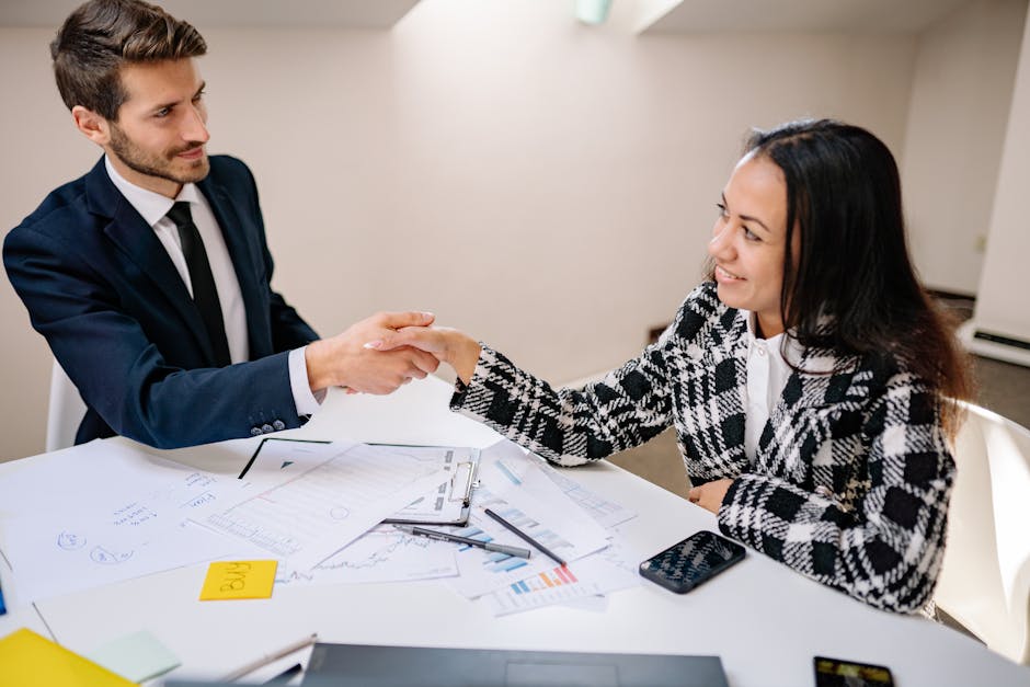 Two business professionals shaking hands over a meeting table, symbolizing cooperation.